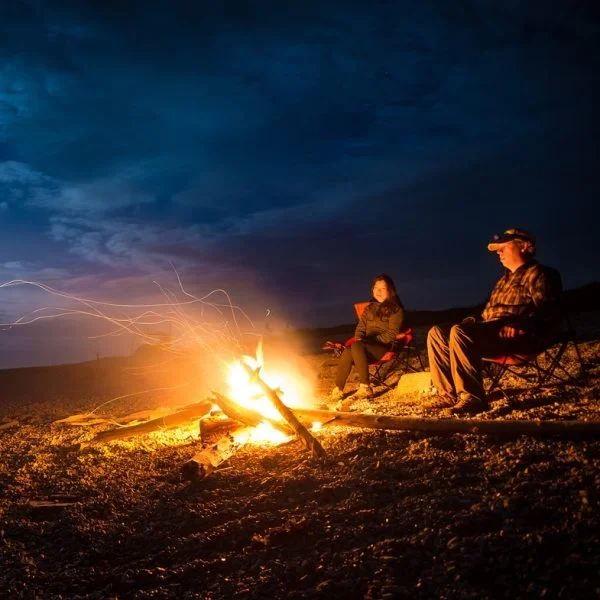 Dos personas sentadas alrededor de un fuego en una expedición de aventura.