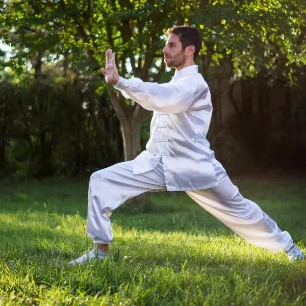 Hombre practicando Taichí al aire libre vestido con un traje blanco.